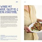 CHICKEN WINGS MIT HONIGGLASUR, GALOTYRI & PEPERONCINI-KRÄUTERÖL. Rezept und Frauenhände halten Teller mit Chicken Wings.