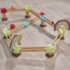 Text „Haba“ auf Bausteinen. Holzkugelbahn mit bunten Schienen, Bällen und dekorativen Elementen wie Regenbogen und Baum.