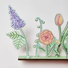 Illustration von stilisierten, bunten Blumen mit erhabenen Punkten auf grünem Sockel.