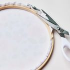 Text auf Schere: "RICCI". Eine Stickrahmen mit eingespanntem Stoff, daneben eine weiße Griffschere.