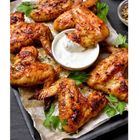 Knusprige Hähnchenflügel auf Pergament, serviert mit einer Schale weißem Dip, garniert mit grünen Kräutern.