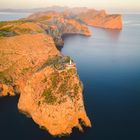Eine Landzunge mit steilen Klippen ragt in das ruhige Meer. Auf der Spitze steht ein Leuchtturm.
