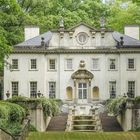 Ein großes, elegantes Gebäude im klassischen Stil, umgeben von üppigem Grün und mit symmetrischer Fassade.