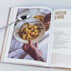 „Tortellini in Brühe“ und ein Rezepttext. Zu sehen ist ein Teller mit Tortellini, eine Suppenkelle und ein Löffel.