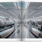 Texte: "FISSION BATTERY". Eine futuristische Fabrikhalle mit großen Maschinen und Personen in Arbeitskleidung.