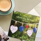 Text: "Die allerbesten Wünsche für dich! 2027. 12 Wünsche für ein tolles Jahr." Kalender mit hängenden Herzen draußen.