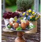 12. März. Mo 22 Di 23 Mi 24 Do 25. 

Braune Eier in einem Metallständer, dekoriert mit Frühlingsblumen und grünen Zweigen. Dahinter bunte Blumentöpfe.