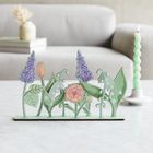 Keine erkennbaren Texte. Illustration von stilisierten Blumen in Pastellfarben auf einem Tisch. Im Hintergrund eine Couch.