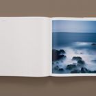 Text: "Cape Verde." 
Ein Fotobuch zeigt ein Meer mit sanften Wellen, das Steine umspült.