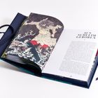 Text: „AUS SCHLEIM GEBOREN“. Ein geöffnetes Buch mit einer Illustration, die eine Figur in einem wilden, naturhaften Szenario zeigt.