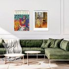 Text: "MATISSE". Zwei farbenfrohe Kalender an der Wand über einem grünen Sofa und zwei runden Tischen.