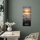 2027. Spirit of Earth. Ein Kalender mit Sonnenuntergang über Wasser, Blumen im Vordergrund, hängt an einer grünen Wand.