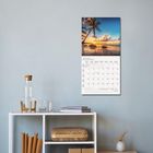 JANUAR 2022. Ein Kalender mit einem tropischen Sonnenuntergangsbild hängt über einem weißen Regal mit Dekoartikeln.