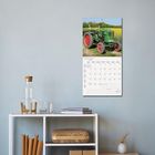 Juni 2023. Kalenderbild mit einem grünen Traktor auf einem Feld. Darunter ein Tisch mit Flasche und Bücher.