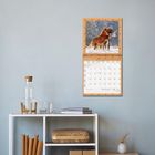 Kalender „Januar 2023“ mit Löwenfoto an der Wand über einem Regal mit Dekoration und Büchern.