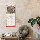 "Bauernkalender für die Familie 2027". Illustration auf Kalender, rustikale Einrichtung mit Uhr, Pflanze und Kissen.