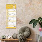 Ein gelber Kalender mit "TIMER FOR 2" für 2027; darunter Tabellen mit Namen und Terminen. Dahinter eine verblasste Wand.