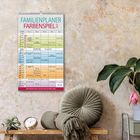 Familienplaner Farbpenspiel 2024. Mit Ferienübersicht und Vorschau bis März 2025. Kalender hängt an beiger Wand, daneben Pflanzen.