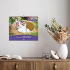 "SamtPFOTEN 2024" zeigt ein Kätzchen in einem Korb. Darunter ein Holzregal mit Büchern, Vase mit Trockenblumen.