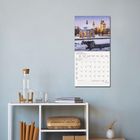 Kalenderblatt mit "JANUAR 2027". Schneebedecktes Gebäude mit Lichtern. Minimalistische Wohnungseinrichtung darunter.