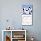 Kalender mit Januar 2027 zeigt Pinguine. Darunter ein Tisch mit Büchern, Flasche und geflochtenem Korb.