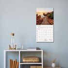 Der Kalender zeigt den Mai 2027. Darunter ein Holzsteg zu Felsen im Sonnenuntergang. Ein Regal mit Büchern und Karaffe.