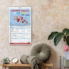 "Unsere Familie ist die beste der Welt" steht oben. Darunter ist ein Familienkalender an einer Wand. Rechts Pflanzen.
