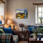 Text: "2024 SCHOTTLAND", "REISEN SINNEN".  
Ein Wohnraum mit Kamin, gemütlichen Sofas, Plaids und Blumen.