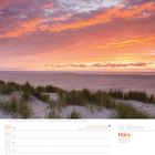 10. Woche März 2027. Sonnenaufgang am Borkumer Strand mit rosa-orangefarbenem Himmel und Gras im Vordergrund.
