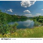 "Juli/August 2027, 30./31. Woche, Aggerstalsperre bei Gummersbach-Lantenbach." Ein See mit Bäumen und Wolken am Himmel.