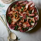 Salat aus Radicchio, Spinat, Parmesan und Orangen. Daneben gestapeltes Porzellan mit Blumendekor auf einer Tischdecke.