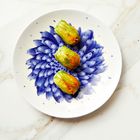 Drei gefüllte Zucchiniblüten liegen auf einem Teller mit blauem Blumenmuster auf weißem Marmortisch.
