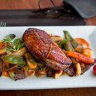 Ein saftiges Stück Fleisch auf Gemüse wie Zuckerschoten, Karotten in brauner Sauce, dekoriert mit Rosmarin.