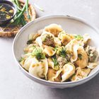 Schale mit gedämpften Dumplings, garniert mit Frühlingszwiebeln, daneben Sojasauce in kleinem Schälchen.
