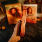 Ein Buch wird aus einem Winkel gehalten, der Rücken ist zur Kamera gerichtet, zwei bunte Buchumschläge im Hintergrund.