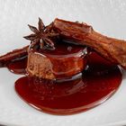 Ein Dessert auf einem weißen Teller, mit einem runden Schokostück, überzogen von Schokoladensauce und dekoriert mit Sternanis.