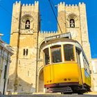 „CARREIRA N.º 12“ steht auf einer gelben Straßenbahn vor einer alten Kirche mit zwei Türmen bei klarem Himmel.