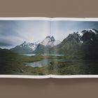 Text: "Torres del Paine 2019". Das Bild zeigt eine weite Landschaft mit Bergen und Seen unter bewölktem Himmel.