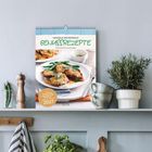 "Saisonale und regionale Genussrezepte 2027." Ein Kalender mit einem Tellergericht darauf, umgeben von Pflanzen.