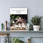 "Literaturkalender Hunde, Fotos von Heike Streil. Drei Welpen kuscheln auf Holz. Umgebung mit Kräutertöpfen und Gewürzmühle."