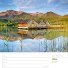 Kalendertext: März 2027, 12. Woche. Bild: Bootshäuser am Kochelsee, Berge im Hintergrund, ruhiges Wasser, klare Himmel.