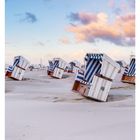 15 APRIL, MO 12 DI 13 MI 14 DO 15 FR 16 SA 17 SO 18. Strand mit Strandkörben bei blauem Himmel und rosa Wolken.