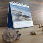 Ein Tischkalender zeigt ein Foto von einem Strand mit einem Zitat: "Wenn wir nicht bewusst auf eine Menge Dinge verzichten..."