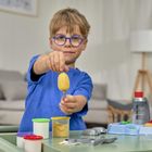 Ein Kind mit blauer Brille zeigt bunte Knete auf einem Tisch mit Spielzeug.