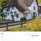 Kopp's Spezialitäten. Reetgedecktes Friesenhaus mit weißer Fassade und blühenden Sträuchern im Vordergrund.