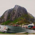 Boote am Dock vor einem großen, grünen und grauen Berg mit kleinen bunten Häusern am Wasser entlang.