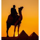 17 APR/MAI. Wüstenlandschaft mit Mann auf Kamel vor Pyramiden im Sonnenuntergang.
