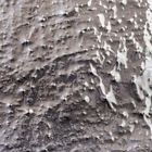 Abstraktes Gemälde mit einer grauen, strukturierten Oberfläche, die von weißen, fließenden Mustern überlagert wird.