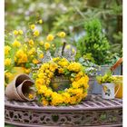 18 MAI MO 03 DI 04 MI 05 DO 06 FR 07 SA 08 SO 09. Gelbe Blumenkränze und Töpfe auf einem dekorativen Metalltisch.