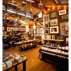 18 MAI, Kalenderansicht. Ein Raum mit Holzinventar, Büchern, Bildern und hängenden Objekten.